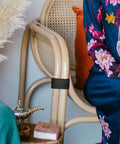 Black adjustable sofa connector securing a wicker chair arm, part of the Four Pack Outdoor Furniture Clips For Woven Sectionals set.