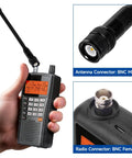 Close-up of a hand holding a radio with a BNC Dual Band Handheld Scanner Antenna 2 Pack Flexible 6 Inch for VHF UHF connection details.