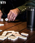 Rambler 20 Oz Tumbler Stainless Steel Vacuum Insulated With MagSlider Lid Black next to domino game on wooden table