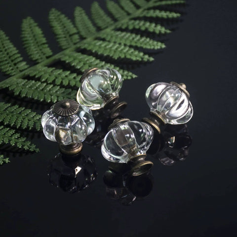 Four clear acrylic pumpkin cabinet knobs with metal bases displayed against a dark background with greenery, showcasing vintage style.