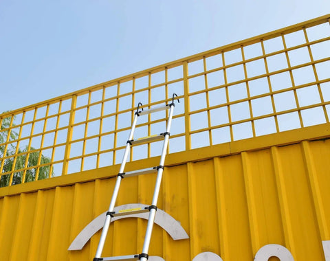 Telescoping Aluminum Ladder 15 Ft For Home DIY And RV Attic Access leaning against a tall yellow structure outdoors