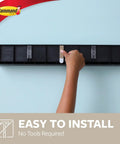 Hand installing Damage Free Picture Ledge 21 Inch Floating Shelf With Adhesive Strips No Tools Needed Holds Photos And Decorations Up To 5 Pounds Slate Finish Includes 1 Ledge And 10 Strips on wall