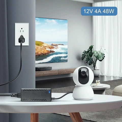 12V 4A 48W AC DC Power Supply Adapter powering indoor camera via 5.5x2.5mm jack, plugged into wall outlet in living room.