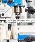 Blue drill press in a workshop; gloved operator adjusts the spindle over a clamped metal workpiece.