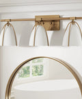 Modern vanity wall fixture above mirror in matte gold with three white metal shades.