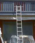 Heavy-Duty Ladder Stabilizer With Wing Span Wall Standoff for Extension Ladders, attached to a house gutter, used in roofing.