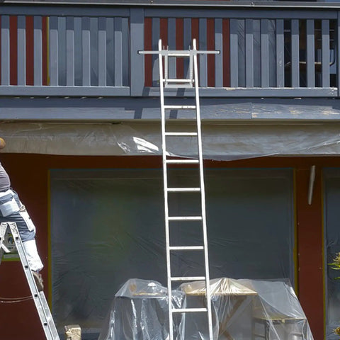 Heavy-Duty Ladder Stabilizer With Wing Span Wall Standoff for Extension Ladders, attached to a house gutter, used in roofing.