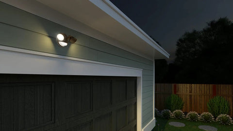 HomeGuard Two Light Outdoor LED Flood Lights With Motion Sensor Dusk To Dawn Auto On mounted on a garage wall at night