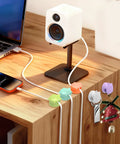 8 Pack Rotatable Cable Clips For Desk, Nightstand, Car And Wall Mount holding cables on a wooden desk near a laptop and speaker