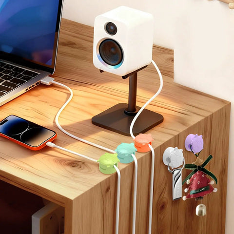 8 Pack Rotatable Cable Clips For Desk, Nightstand, Car And Wall Mount holding cables on a wooden desk near a laptop and speaker