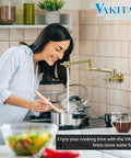 Woman using gold pot filler wall mount faucet with double joint swing arm in kitchen, high flow brass construction.