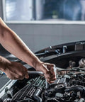 Drive converter sleeve adapter (1/4–1/2 in) in machined alloy; being used with a socket wrench under a car hood.