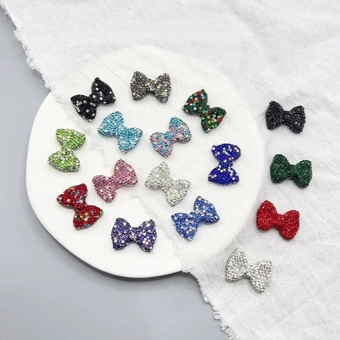60Pc Glossy Black Disco Ball Beads With Sparkly Rhinestone Perfect for Diy Jewelry Crafting Dazzling Necklace Charms or Bracelet Spacers Add Dope Swag to Your Creations 21.5X30Mm Size for Ultimate Bling Effects and Vibe Ups with colorful rhinestone bow-shaped beads on a plate.