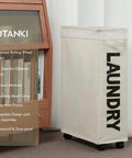 Big Ol Extra Large 27 Inch Slim Rolling Laundry Basket On Wheels With Removable Bag featuring a beige collapsible design next to furniture