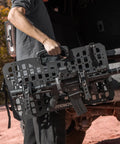Person holding 2 Pack Tactical Gun Rack For MOLLE Panels Automotive Rifle Holder For Cars And Trucks with attached rifle