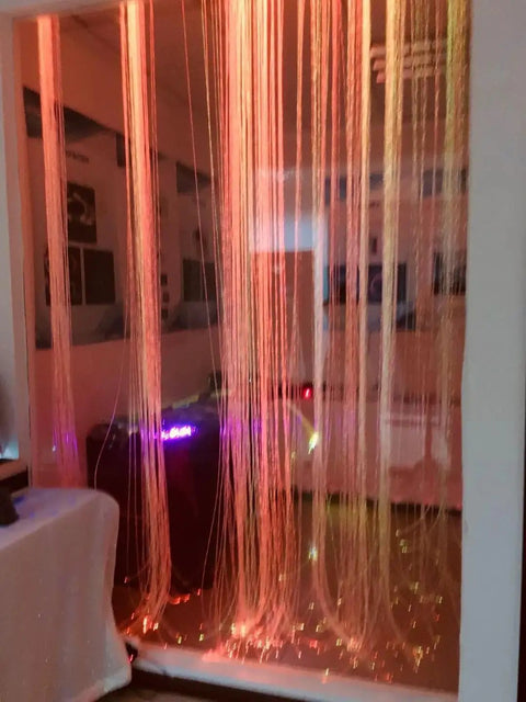 16W RGBW Fiber Curtain Lights Kit For Waterfall Backdrop in a sensory room, glowing in orange hues, with 450 strands of fiber optic cables.