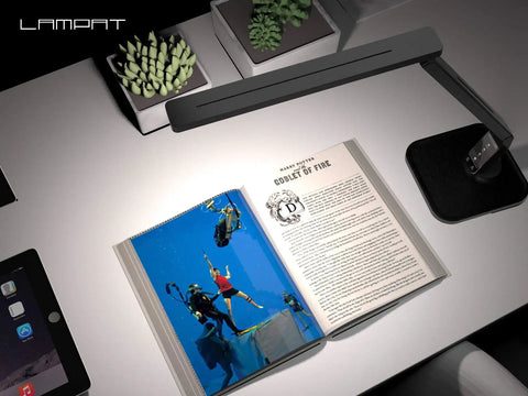 Overhead view of Super Handy Dimmable Led Desk Lamp illuminating a book on a white desk with touch controls, in piano black.