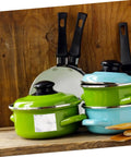 Colorful kitchenware set including green and blue pots with lids and black-handled frying pans against wooden background.