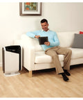 Man sitting on a sofa with AeraMax 300 air purifier beside him, showcasing its fit for modern living spaces.