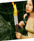 Person holding a lit torch outdoors, featuring a wrapped handle and flame against a green natural background.