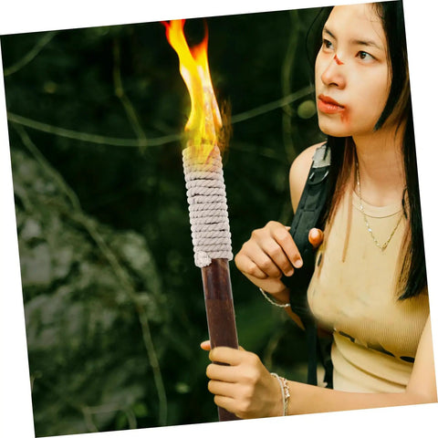 Person holding a lit torch outdoors, featuring a wrapped handle and flame against a green natural background.