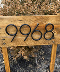 Front view of 5-inch black stainless steel floating house numbers, four digits, mounted on a wooden sign with nail kit.
