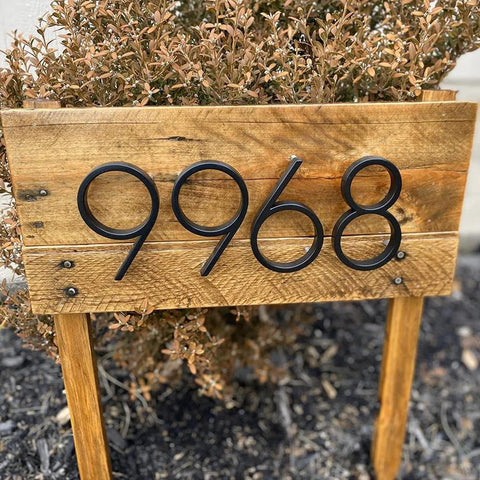 Front view of 5-inch black stainless steel floating house numbers, four digits, mounted on a wooden sign with nail kit.