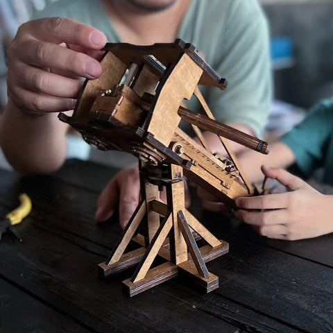 Mini Roman Ballista Siege Engine Kit for Tabletop Battles DIY Wooden Catapult Model 3D Puzzle STEM Project Medieval War Machinery for Kids and Adults Educational Fun and Hands On Building, wooden tabletop model held by hands