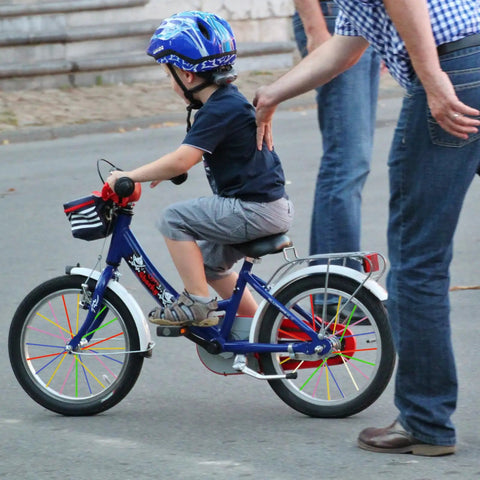 Child on bike with 180 Pcs Spoke Covers Set For Bikes And Dirt Bikes, 10 Color Variety on wheels, adult guiding.
