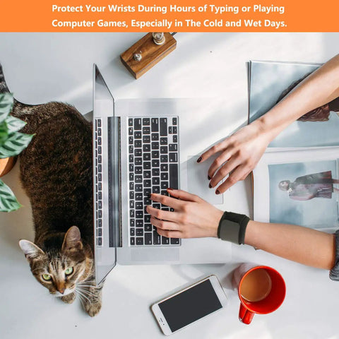 Person typing on a laptop with 2 Pack Wrist Wraps For Carpal Tunnel Relief And Pain Prevention, cat nearby, and coffee cup on desk.