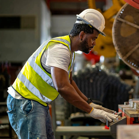 Worker wearing Men's Yellow Solid X Large Modern Safety Vest with 9 Pockets, focusing at a workbench in an industrial setting