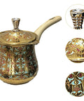 Ornate brass milk warmer and coffee pot with long handle, featuring intricate designs, shown from a side angle.