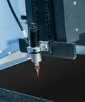 Close-up of laser engraving machine head with pink-tipped nozzle over dark work surface