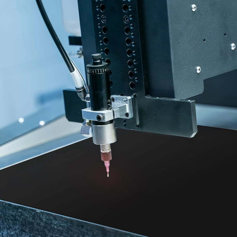 Close-up of laser engraving machine head with pink-tipped nozzle over dark work surface