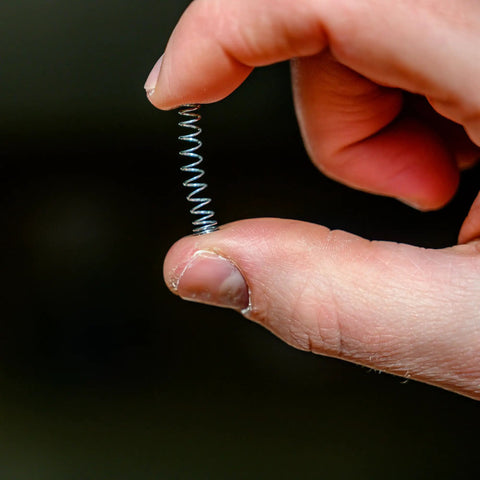 Person holding a small spring between fingers, showcasing the compression and coiling of the wire.