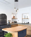 Modern farmhouse kitchen with Three Light Black Pendant Light With Seeded Glass Shades above wooden island and black stove.