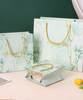 Set of three green floral paper bags with gold handles in varying sizes for gifts