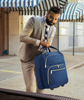 Man holding Underseat 16-Inch Carry-On Luggage With Wheels, Softside Rolling Travel Bag, blue quilted design, outdoors