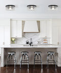 Modern kitchen with silver bar stools and white cabinets, featuring three ceiling lights above the island.