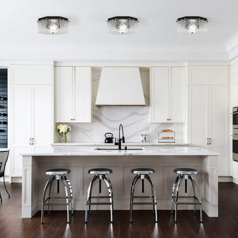 Modern kitchen with silver bar stools and white cabinets, featuring three ceiling lights above the island.