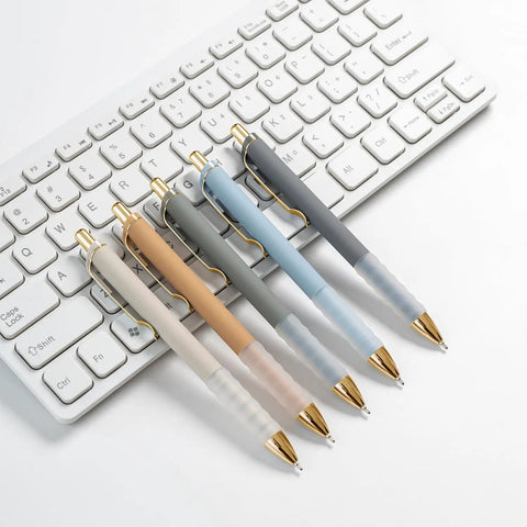 Gold 12 Pack Retractable Ballpoint Pens With Ultra Soft Grip 1.0mm Point Smooth Black Ink placed on a white keyboard