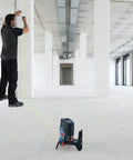 Pro Level 12V Green Beam Cross Line Laser With 100 Foot Reach and Smart Visimax Tech aligned with a vertical wall in a spacious interior.