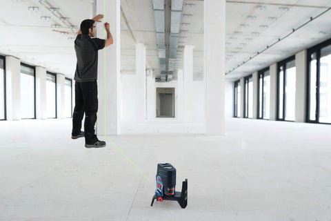 Pro Level 12V Green Beam Cross Line Laser With 100 Foot Reach and Smart Visimax Tech aligned with a vertical wall in a spacious interior.