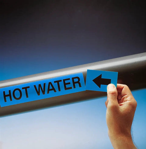 Hand applying a Top Shelf Self Stick Compressed Air Pipe Marker 1X8 Inch White On Blue to hot water piping.