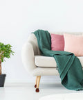 Sofa with brown wooden bun style legs, green blanket, pink cushions, plant beside, showcasing Brown Wooden Bun Style Sofa Legs Replacement Set Of 4 Dope Sturdy Furniture Feet For Sofas Cabinets And Tables Easy To Install For Home Makeover And Refurbishment Projects.