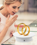Spill Your Secrets With This Hype BESPORTBLE 360 Auto Rotating Display Stand showcasing two gold rings in a jewelry store.