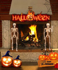 Indoor Halloween Skeletons Two Pack 15 Inch Life Size Full Body Posable Joints Skeleton Figures For Spooky Home Decor Realistic Resin Bone Color Dress Up Ready For Parties And Year Round Halloween Vibe standing near a fireplace.