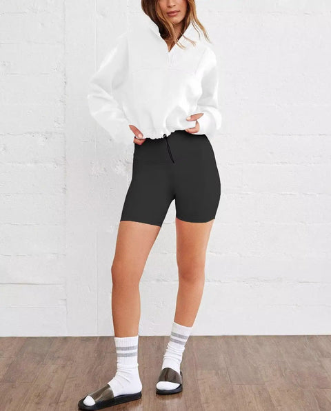Model wearing Women's Cropped 1/4 Zip Sweatshirt Hoodie With Kangaroo Pocket Lightweight Half Zip Pullover Cozy Relaxed Fit Long Sleeve Top For Fall And Winter Y2K Style White Large with black shorts, standing against a white wall.