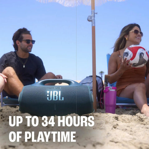 Two people sitting on a beach with a black Hardest Hitting Portable Waterproof Speaker With Pro Sound And AI Boost between them.