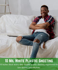Person on couch covered with White 10 Mil Heavy Duty Plastic Sheeting Polyethylene Film For Drop Cloths And Vapor Barrier Painter Tarp Crawl Space Covering Tear Resistant Roll 20 Feet By 100 Feet Durable Multi Purpose Sheeting